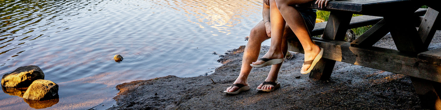 Man and woman wearing Tread Labs sandals sitting at a picnic table by a lake at sunset