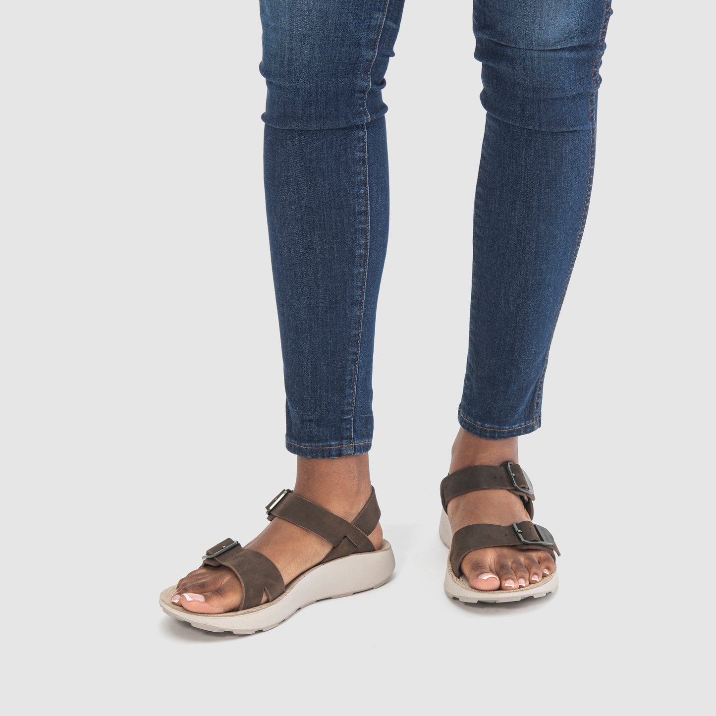 Female model wearing Salinas Leather Sandals in Havana with blue jeans on a white background