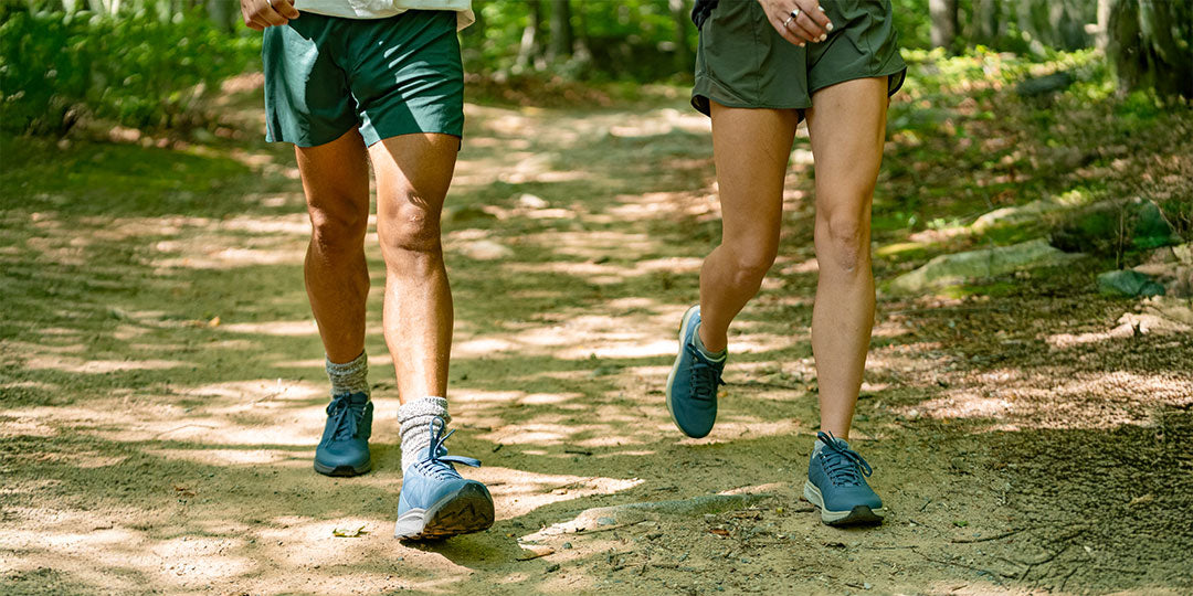 Two people walking on a forest path wearing green shorts and blue Dover RS shoes.