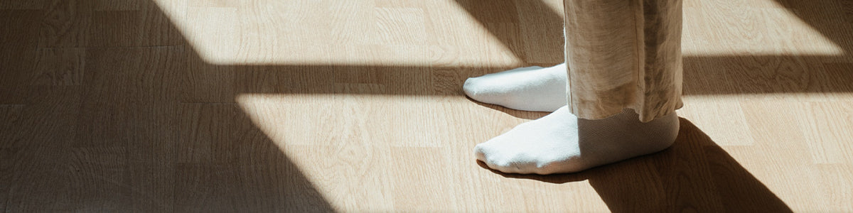 A person's stocking feet standing in the light of a window on hardwood flooring