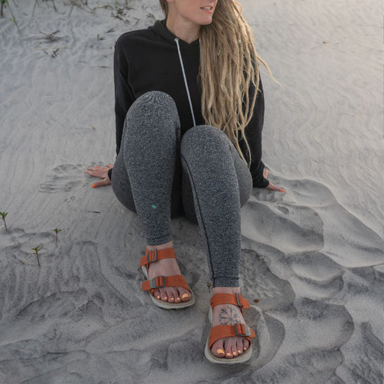 Woman wearing Salinas Sandals in Apricot sitting in the sand at a beach.