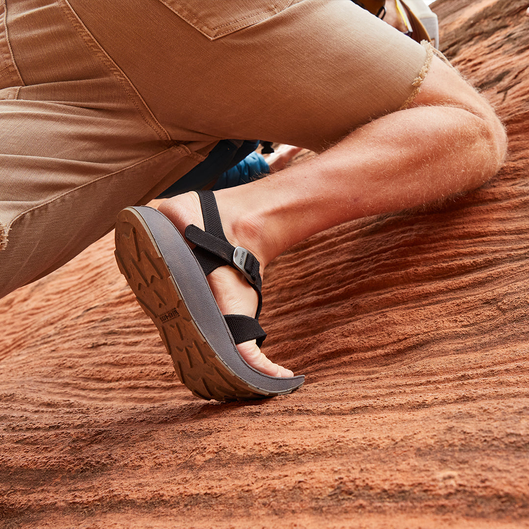 Man wearing black Albion Sandals hiking up a red rock face in Moab, Utah
