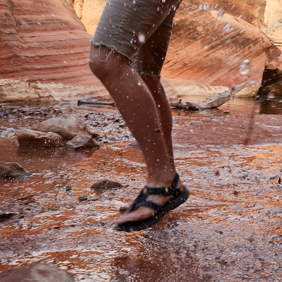 Man wearing Albion Sandals walking and splashing through shallow water in Moab canyon