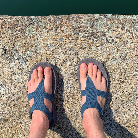 POV of man wearing Men's Albion Sandals on a stone wall by a reservoir of water