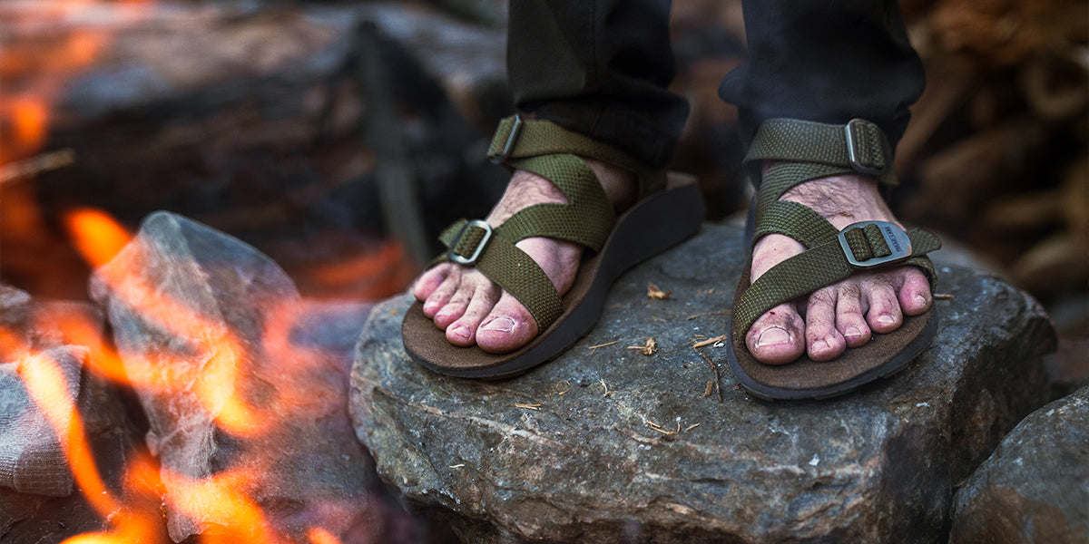 Man wearing Men's Redway Sandals standing on a rock nearby a campfire