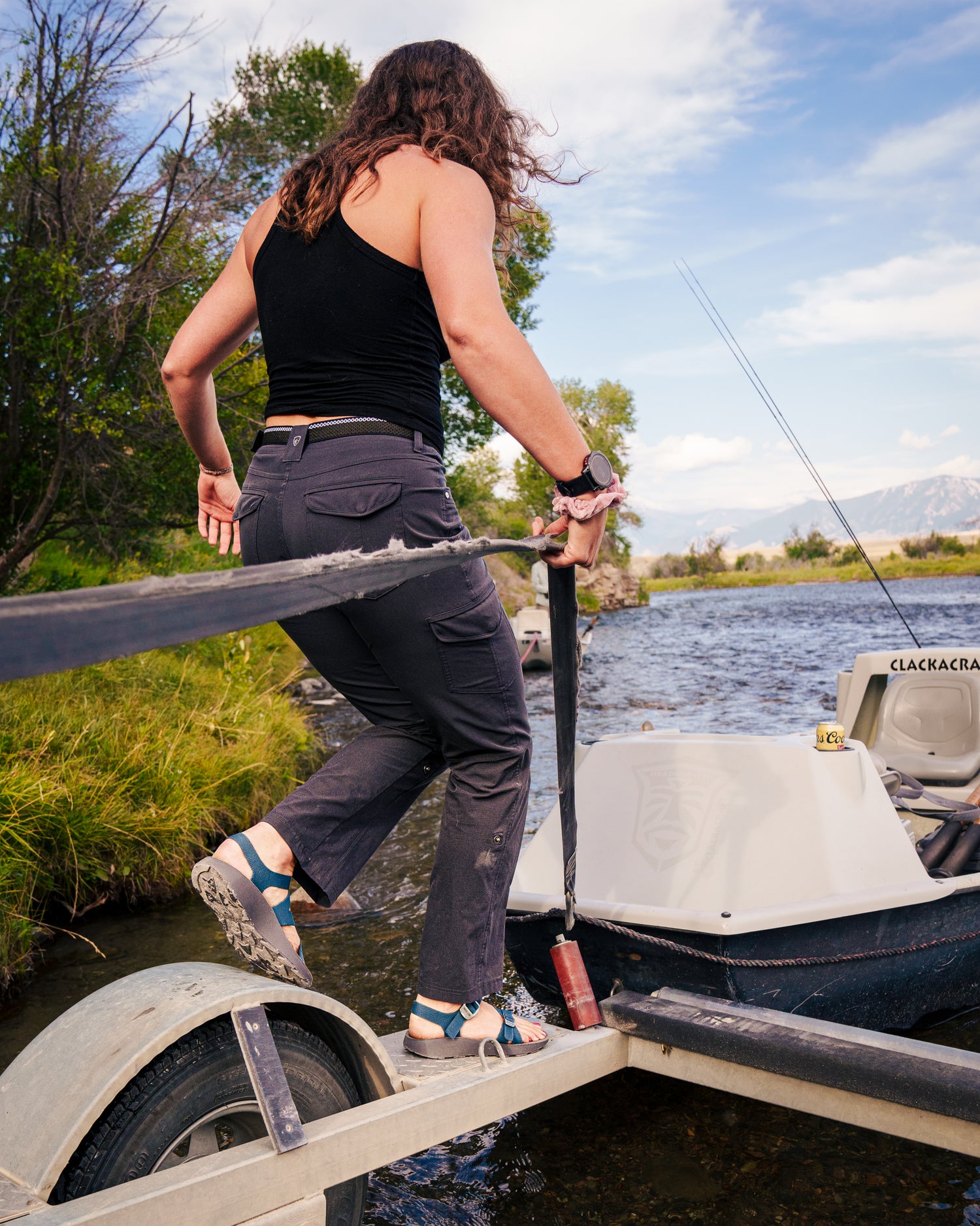 A woman boarding a drift boat on a mountain river.