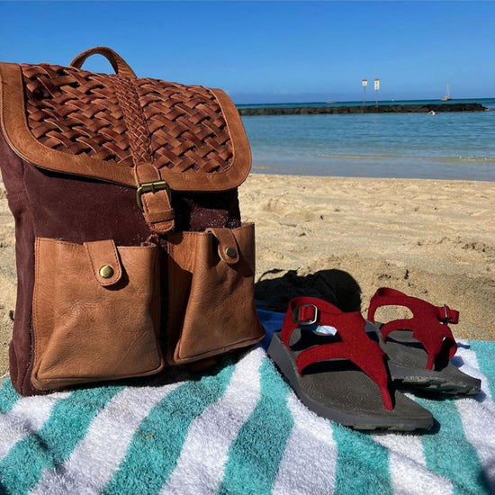A pair of red Albion Sandals next to a leather bag at a sandy beach