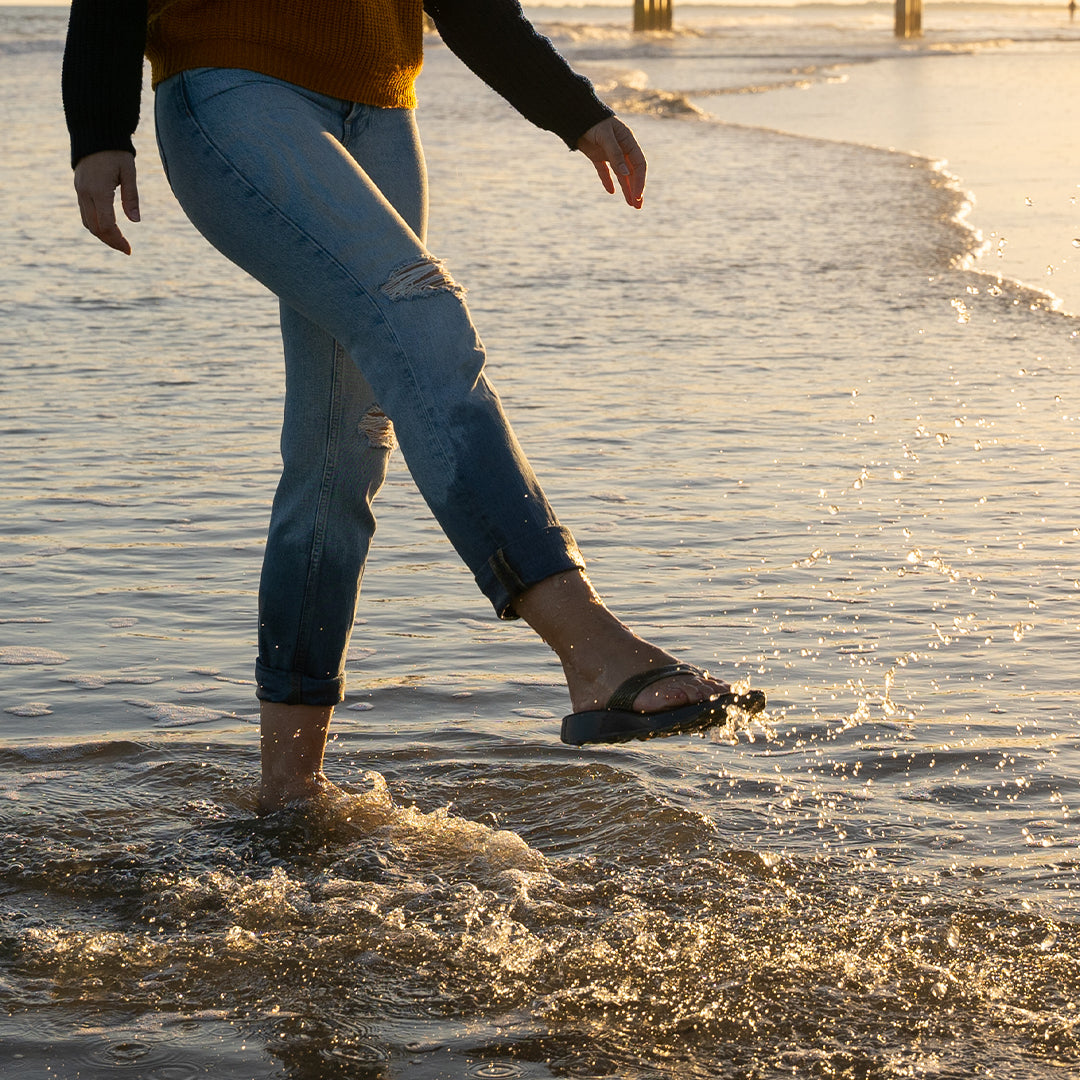 A woman in flip flops splashing water in the ocean surf.