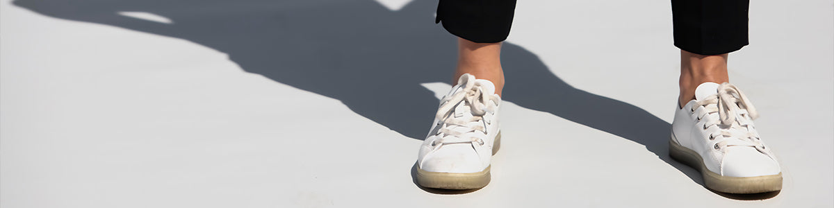 A person wearing white walking shoes standing on concrete