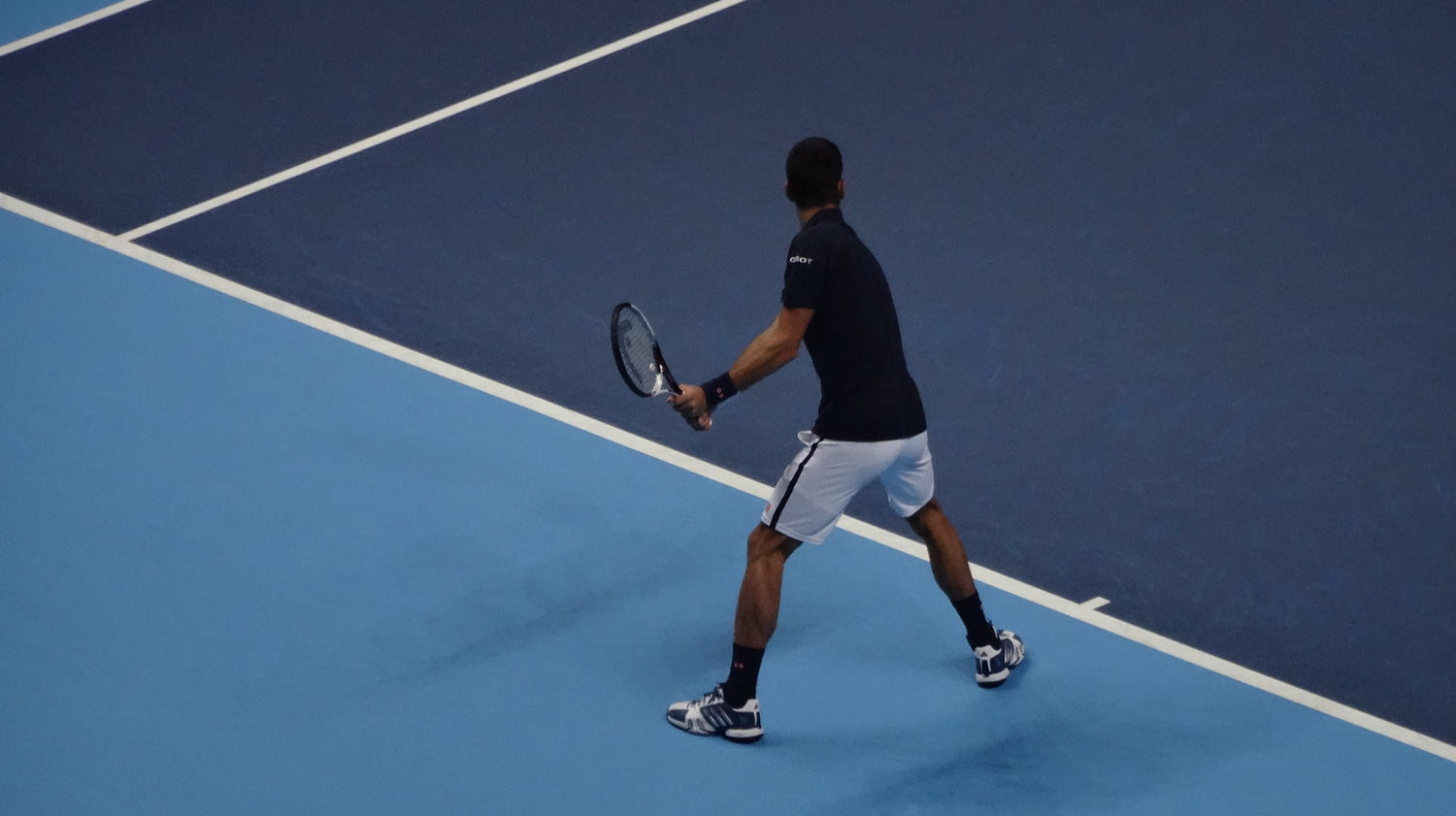 Man on a tennis court getting ready to return a serve from an opponent