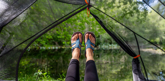 Women's feet wearing Tread Labs Covelo raised in the air, framed by the open door of a mesh tent with trees in the background.