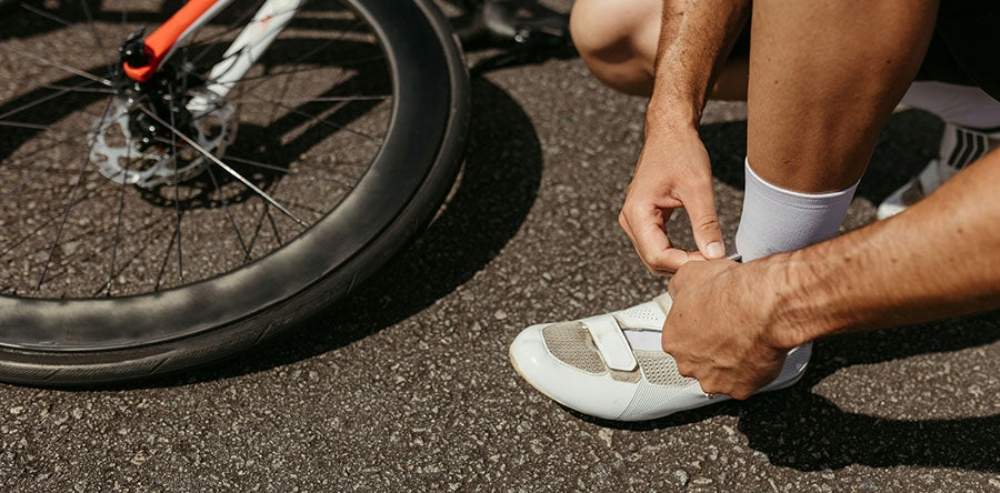 Man crouching down to adjust this cyclig shoe next to his bicycle.