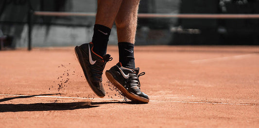 Two feet wearing Nike shoes in motion on an orange court.