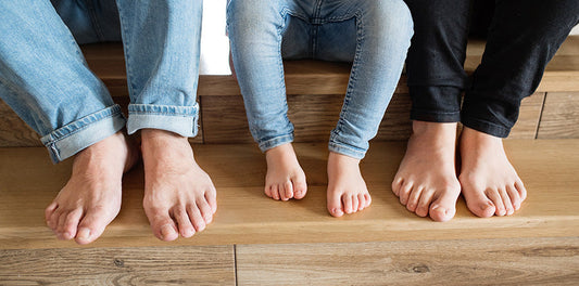 Three pairs of barefeet on a wood floor.