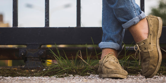 Man standing outside by a fence wearing blue jeans and brown leather boat shoes.