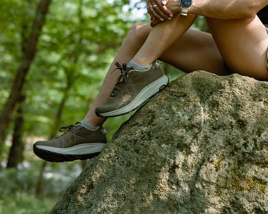 Person wearing brown hiking shoes sitting on a rock with a natural background