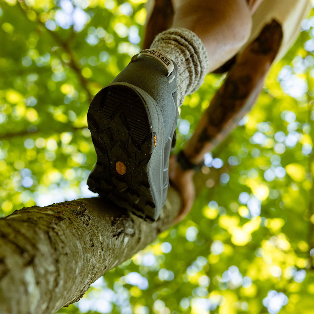 Person climbing a tree wearing a gray hiking shoe with a blurred green forest background
