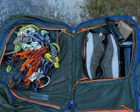 Open green backpack with climbing gear and shoes on a concrete surface