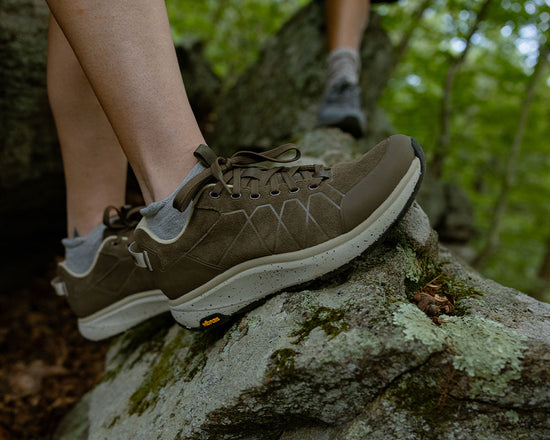 Brown hiking shoes on a rocky surface with greenery in the background