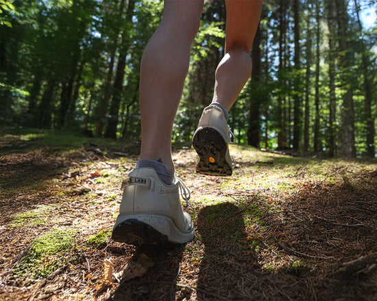 Person hiking on a trail in a forest with focus on their shoes.