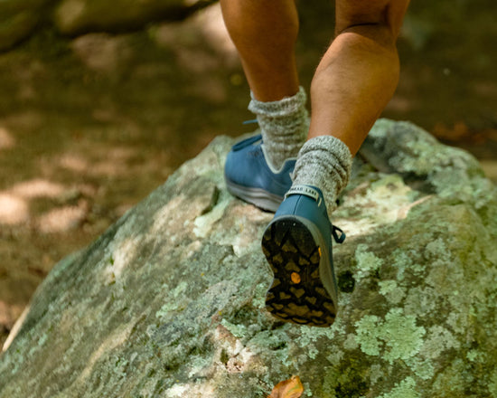 Person wearing blue shoes with black soles climbing a rock in a forest setting