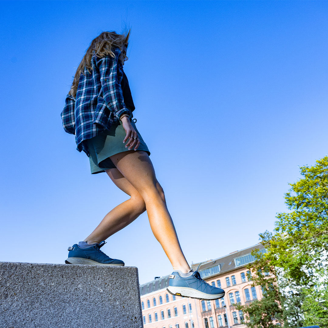 Person standing on a ledge with a clear blue sky and buildings in the background