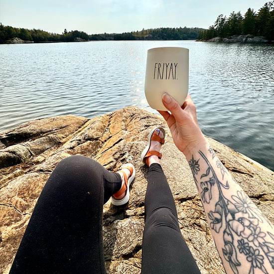 Woman sitting on a rock at an alpine lake wearing Salinas Sandals and holding a white coffee cup.
