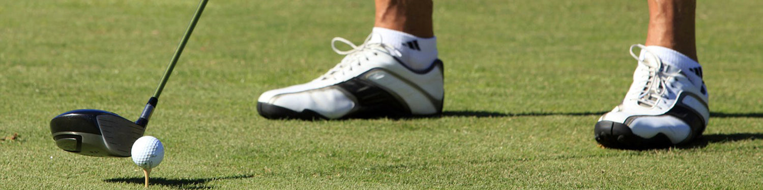 Man wearing golf shoes standing on a golf course preparing to tee off.