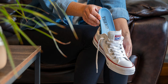 Woman sitting on a leather couch placing Tread Labs arch support insoles into a pair of white Converse All-Stars