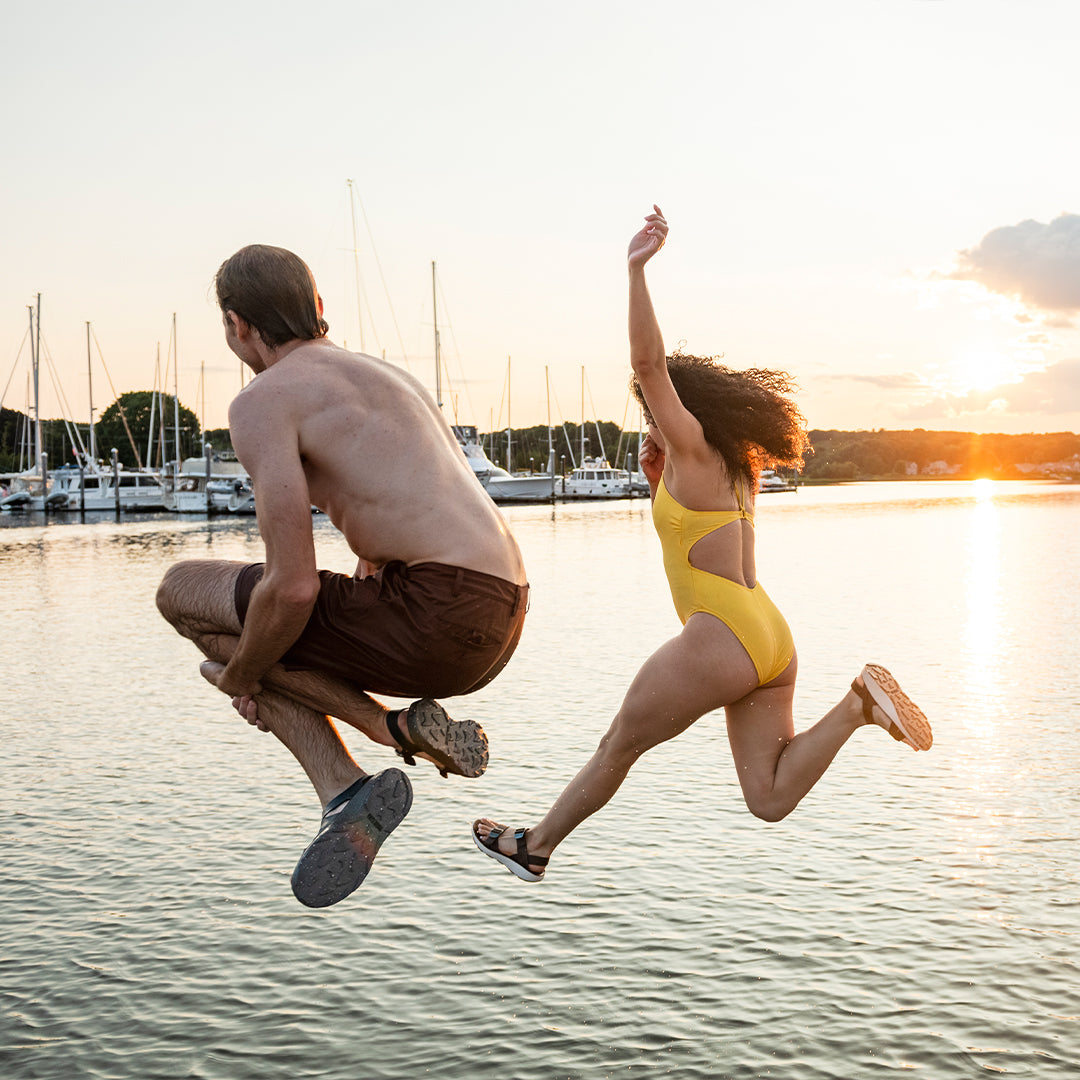 Man and woman wearing Tread Labs sandals jumping off a boat into the harbor at sunset.