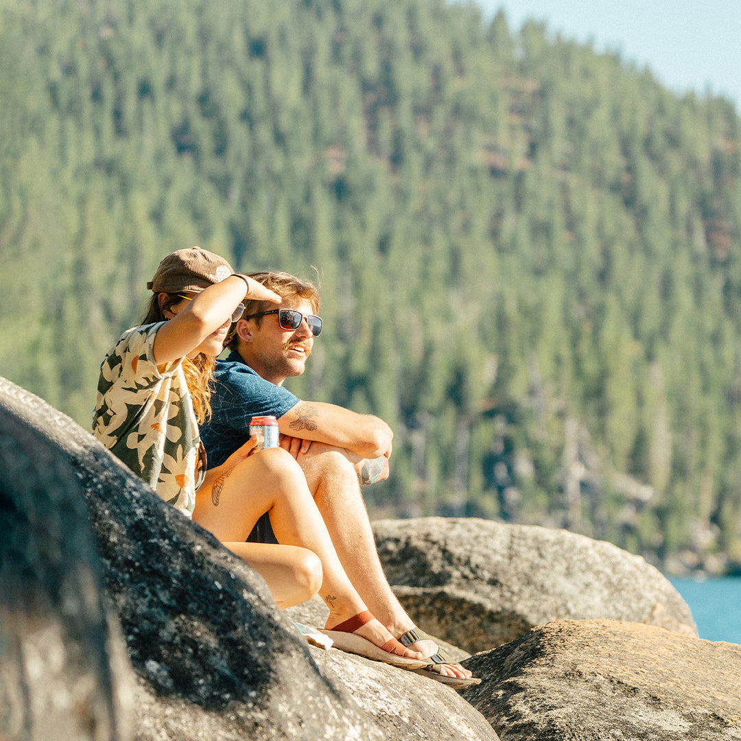 Woman and man wearing Tread Labs sandals sitting on a rock overlooking an alpine lake.