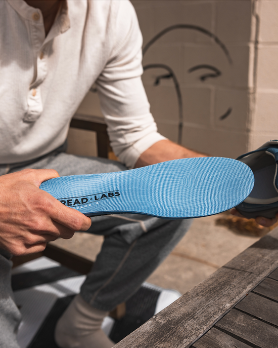 Person holding a blue insole with 'TREAD LABS' branding outdoors.