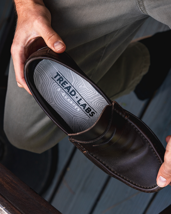 Person holding a brown shoe with 'Tread Labs' branding.