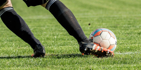 Closeup of soccer player wearing cleats with Tread Labs insoles inside kicking a soccer ball