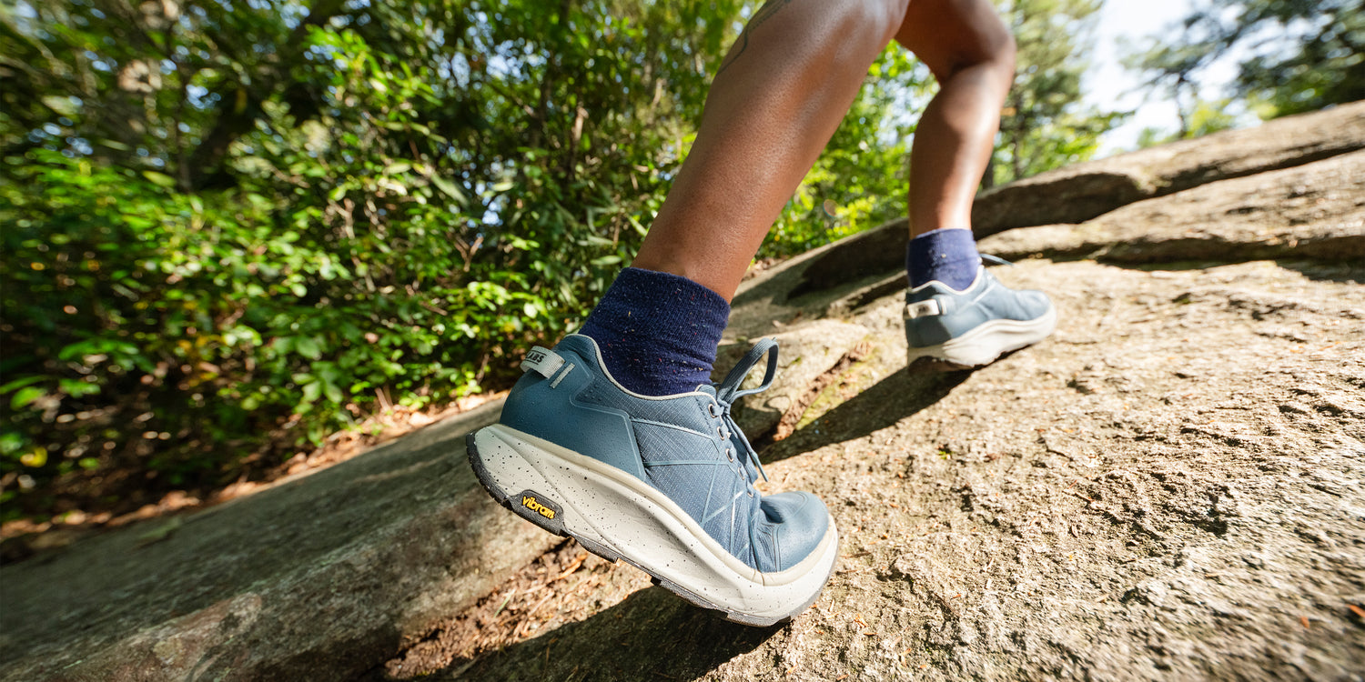 Woman wearing Tread Labs shoes hiking up a sheer rockface.