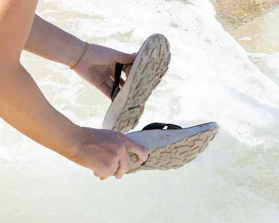 Woman washing off her Tread Labs Orleans Leather sandals in the ocean at the beach