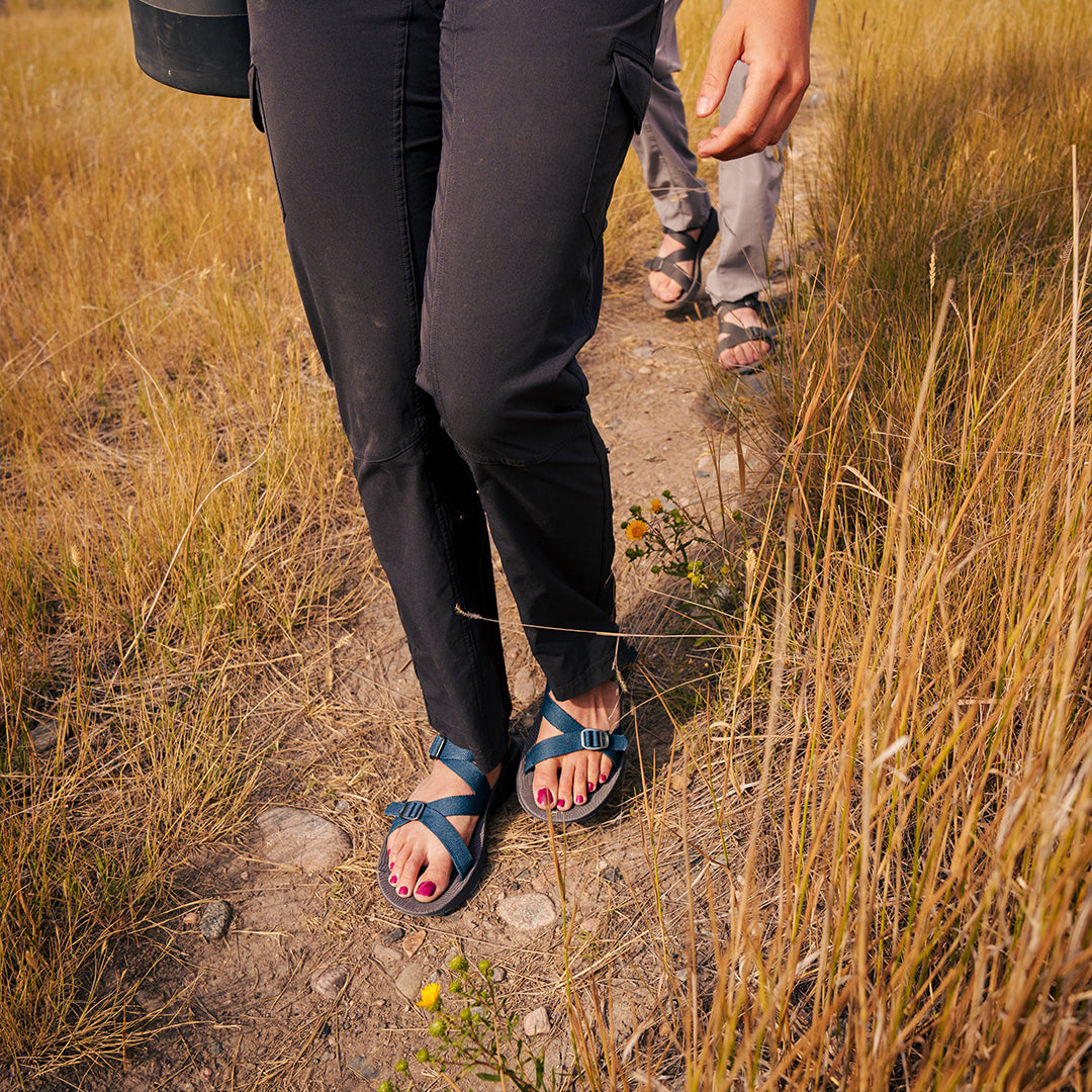 Woman wearing blue Tread Labs Redway Sandals walking along a trail through tall grass.