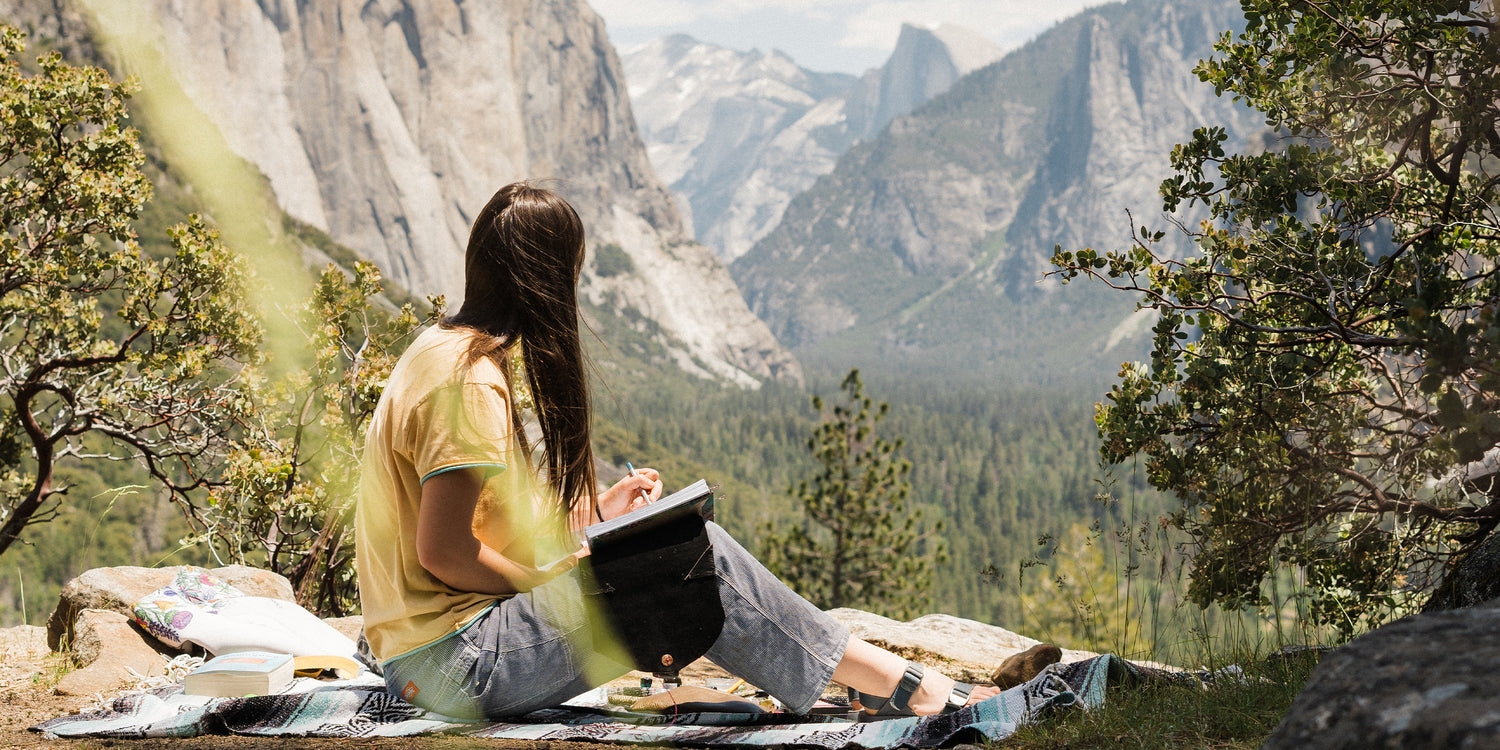 Young woman sitting on a blanket painting a watercolor of the view in Yosemite. She is wearing Tread Labs sandals.