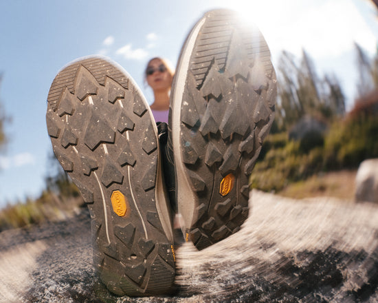 Close-up of hiking shoes with a blurred background of a person on a trail.