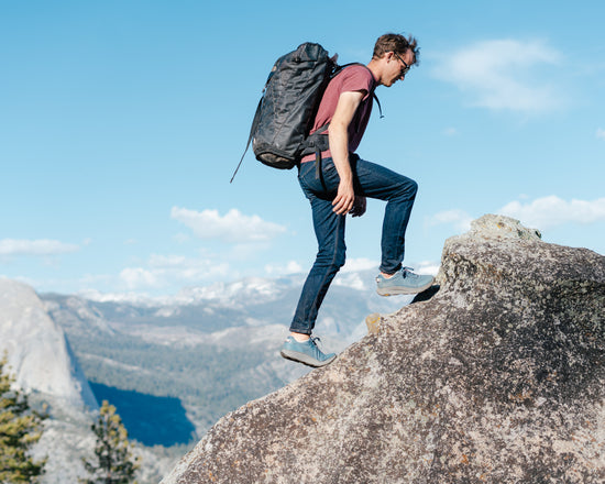 Person with a backpack standing on a rocky outcrop with a scenic mountain view.