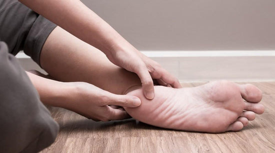 Person sitting on the floor clasping their heel, suffering from plantar fasciitis pain