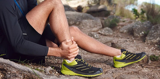 Man sitting on a hiking trail clutching his leg, suffering from tendonitis pain